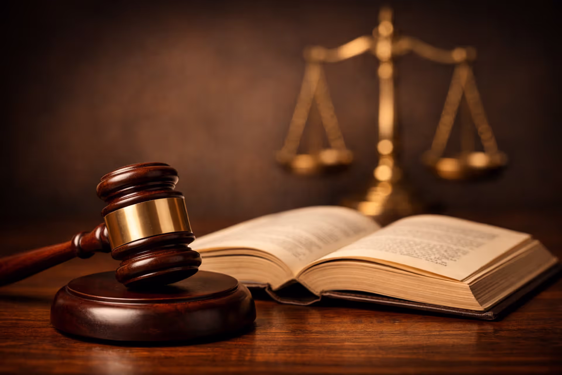 Judge’s gavel resting on a desk next to an open law book with scales of justice in the blurred background