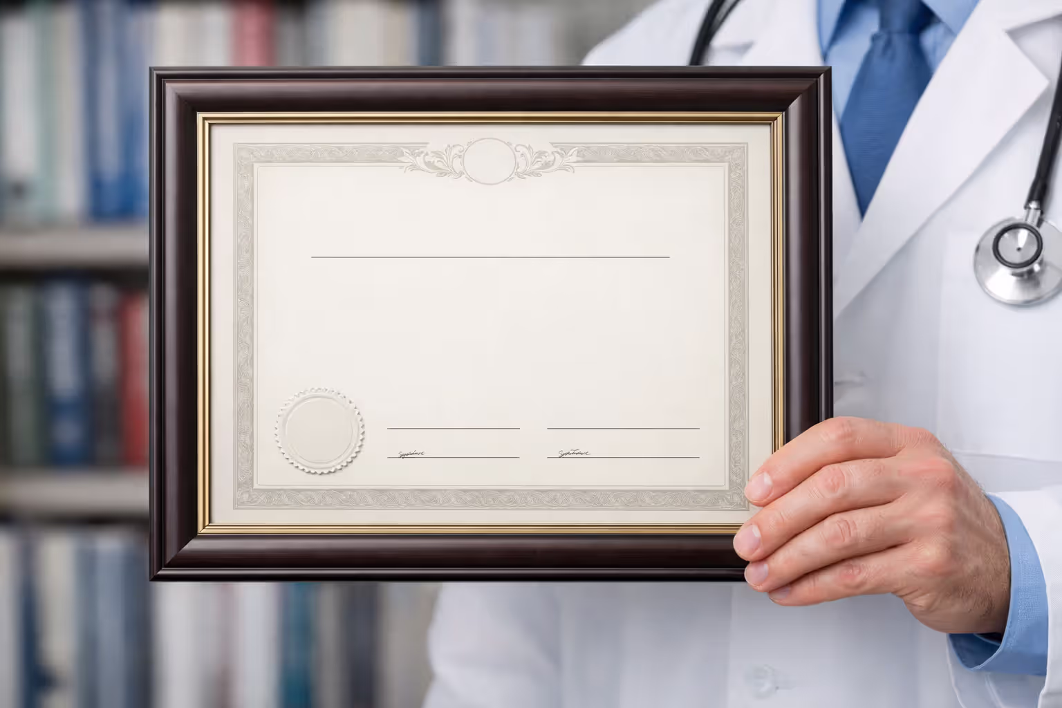 Physician hand holding a framed medical board certification document with blurred bookshelf in background
