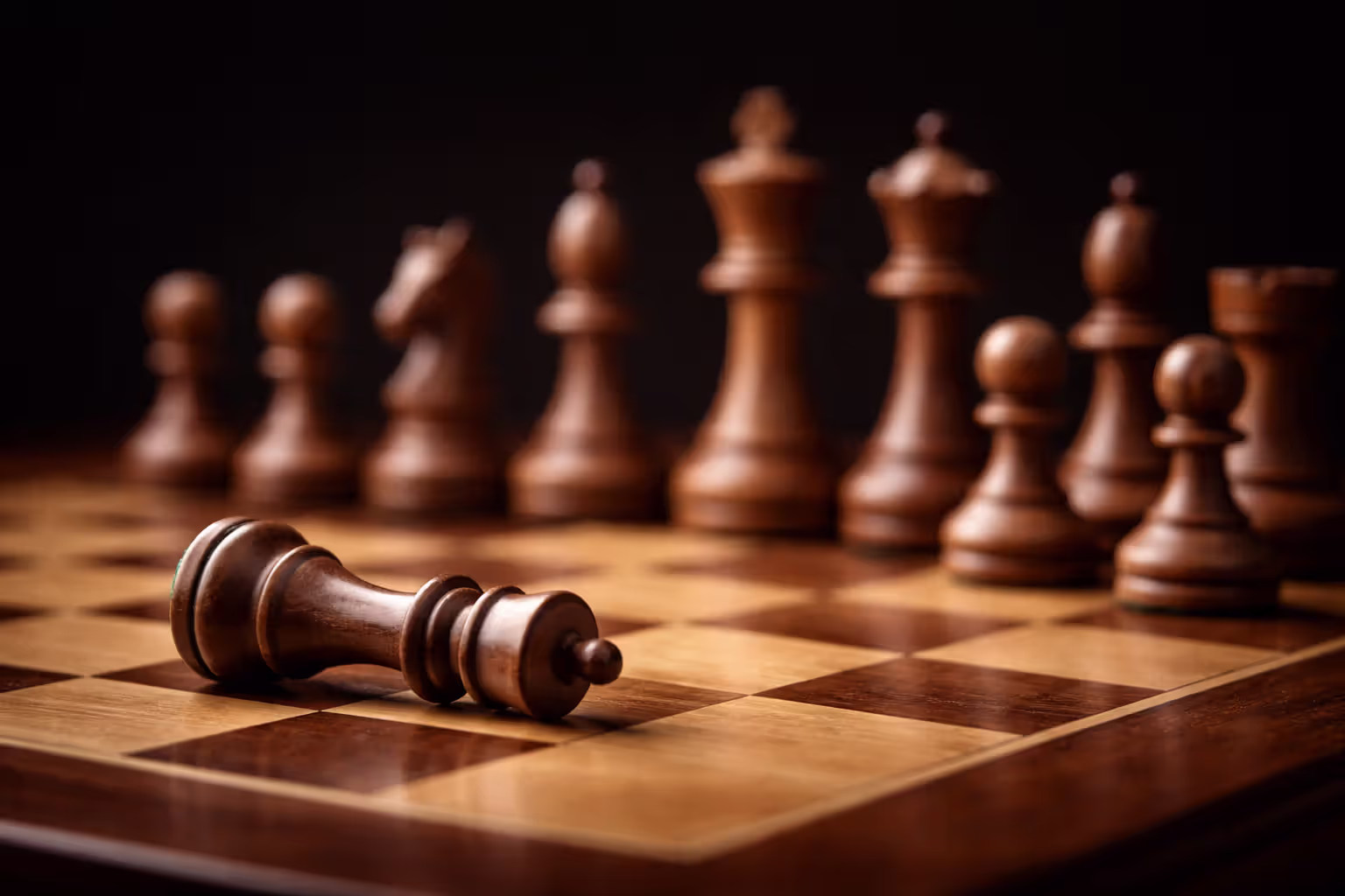 Chess pieces in row on board with one fallen piece symbolizing strategic mistake