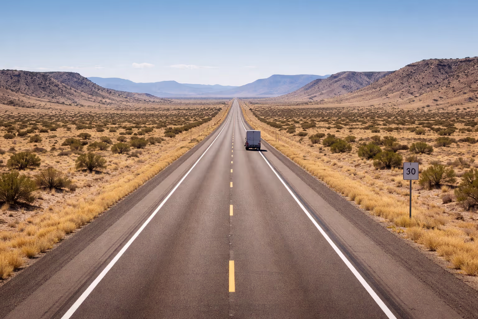 Desert highway in New Mexico with semi-truck driving in the distance and speed limit sign on roadside